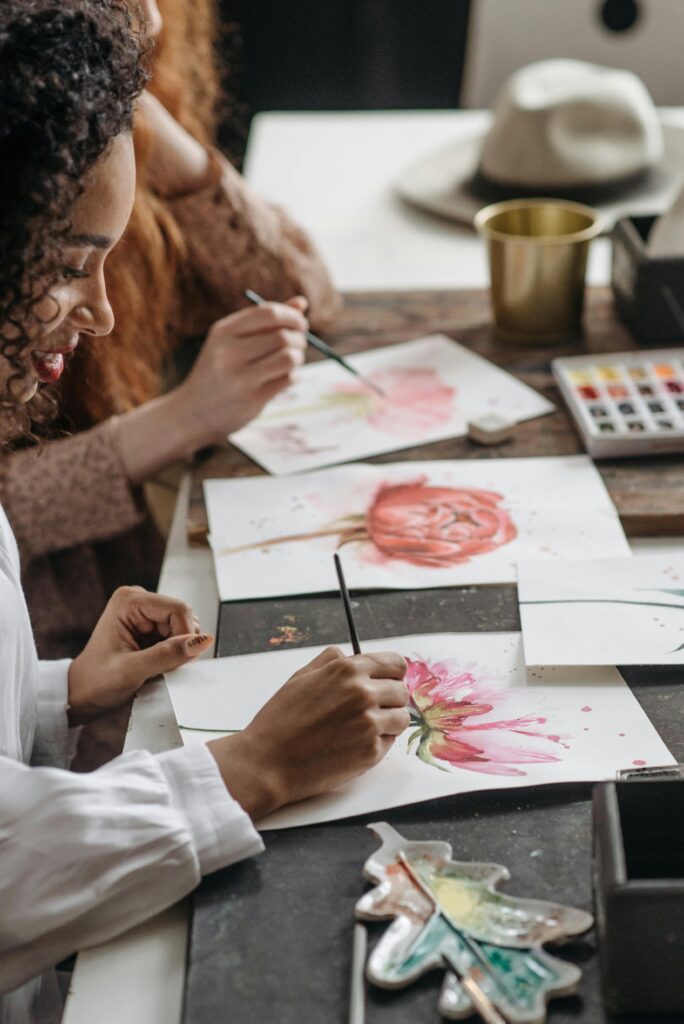 Focused women painting watercolor flowers at an indoor art workshop.